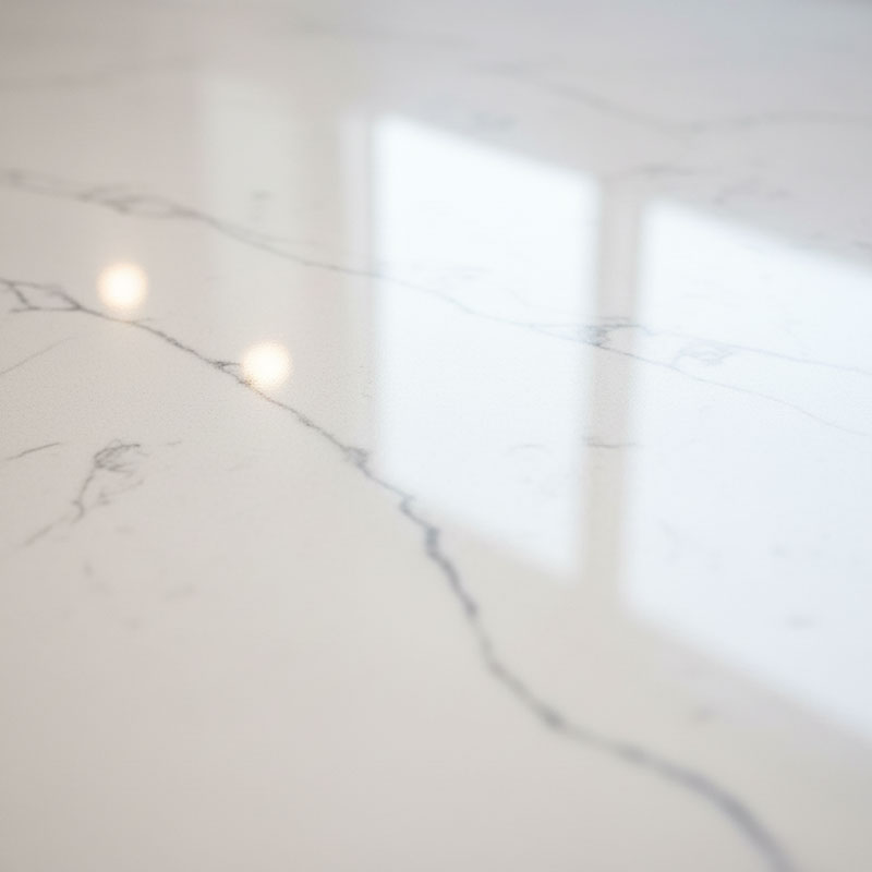 Close-up photograph of polished engineered quartz surface showing mirror-like reflection and visible Calacatta-style grey veining on white background